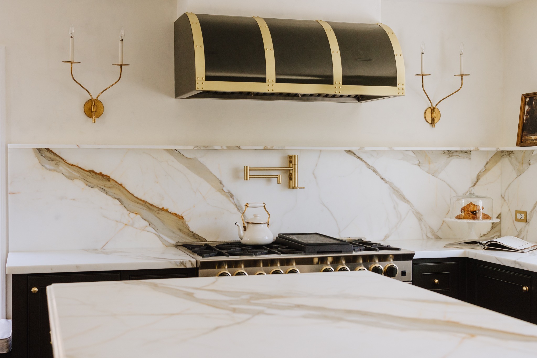 M StudioHouse kitchen with a sculptural brass-trimmed range hood, expressive marble backsplash and brass sconces